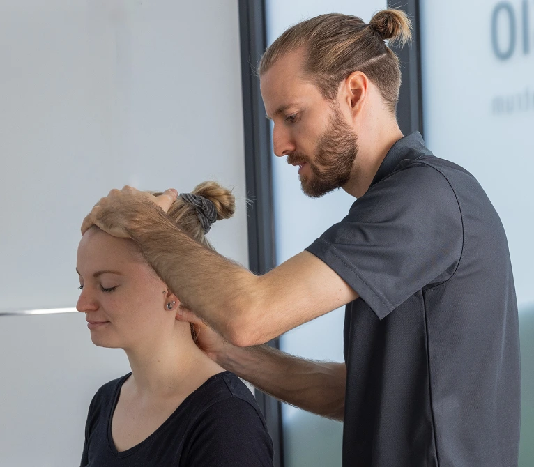 Physiotherapeut führt eine manuelle Nackenbehandlung bei einer Patientin durch.